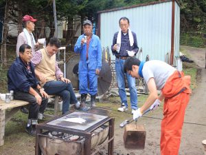 ハウスの外でサンマを焼く。中央が吉田さん